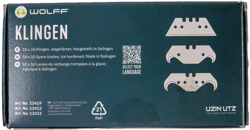 Photographie en gros plan d'une boîte en carton rectangulaire de lames de rechange Wolff pour outils de sol. L'emballage vert foncé montre en haut à gauche le logo 'WOLFF' et, à gauche, le mot blanc en grand 'KLINGEN'. À droite sont imprimées trois illustrations stylisées de lames ; entre les textes se trouve un petit code QR avec la mention 'SELECT YOUR LANGUAGE'. Des informations produit multilingues indiquent en allemand, anglais et français '10 x 10 lames de rechange trempées à la glace ; Fabriqué à Solingen'. En bas à gauche figurent trois numéros d'article et les coordonnées du fabricant, et le symbole de recyclage '21 PAP' apparaît près du bas. Les bords de la boîte montrent de légères traces d'usure. Présentation globale d'un emballage produit propre sur fond blanc.