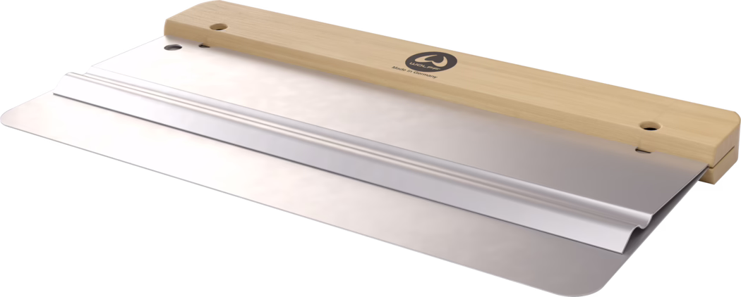 Gros plan d'une large spatule à enduire avec une lame en acier inoxydable polie et un manche droit en bois clair. Le manche porte un logo circulaire 'WOLFF' et l'inscription 'Made in Germany'. La lame métallique présente un raidisseur plié près du bord supérieur et une surface lisse et réfléchissante avec des coins arrondis. L'outil est présenté en léger angle sur fond blanc, soulignant le contraste entre le bois chaud et le métal froid. Conçue pour lisser le plâtre, les adhésifs ou les enduits, la spatule paraît neuve et de fabrication professionnelle.